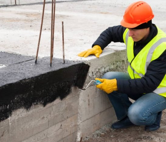 construction worker makes bituminous waterproofing of the foundation at the construction site